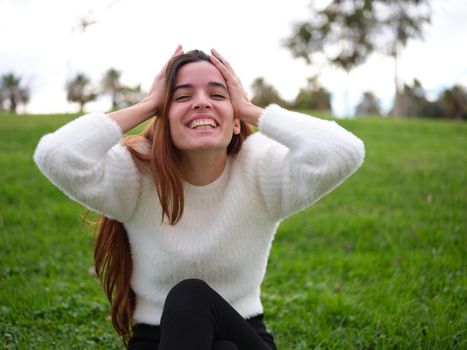 Front view of a happy young girl in the park looking at the camera with her hands on her head having a surprise. Concept of emotions.