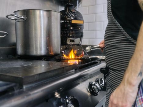 Cropped photo of a chef using metal tongs to remove charcoal from fire in a restaurant kitchen