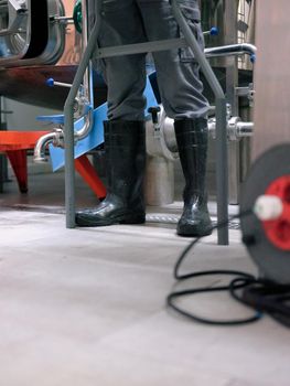Cropped photo of the legs of a worker with protective rubber boots in a brewery