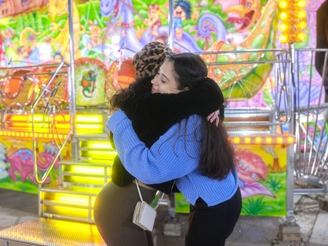 Two friends giving each other a hug in the middle of a colourful night fair