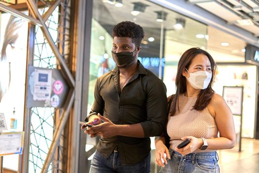 African man and asian woman with facial mask walking in a shopping mall