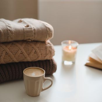 cozy home atmosphere and still life with candle and sweaters on a table.