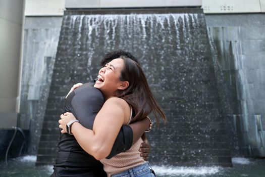 Close up portrait of multiethnic friends embracing next to an artificial waterfall in a modern mall