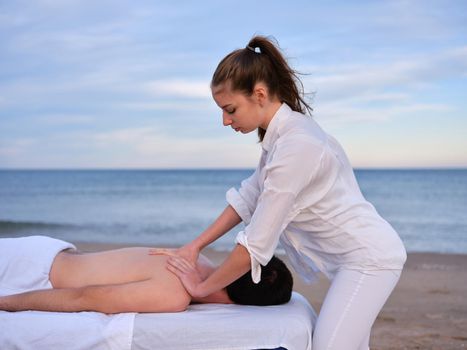 Side view of a chiromassage therapist woman giving a back massage to young man on a beach in Valencia.