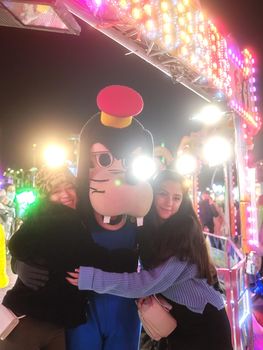 Latina girls hugging an actor dressed like Diseny Goofy dog in a theme park at night