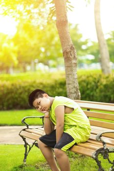 Sport concept - Little sport runner boy sit on the track and take a deep breath. Feel tired and bored.