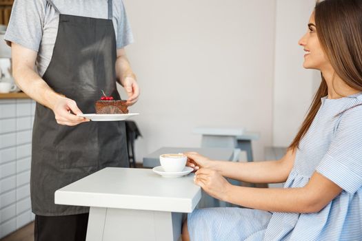 Coffee Business Concept - Waiter or bartender giving chocolate cake and talking with caucasian beautiful lady in blue dress at Coffee shop.