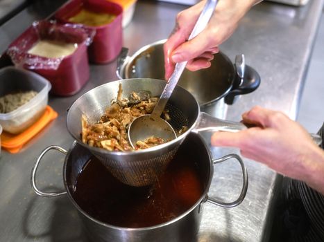 Close up photo of the hands of a chef squeezing juice out of food with a strainer in a restaurant