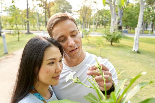 Multicultural couple in love looking at and picking white flowers in an urban park