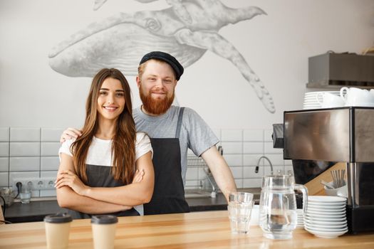 Coffee Business Concept - Positive young bearded man and beautiful attractive lady barista couple enjoy working together at the modern coffee shop