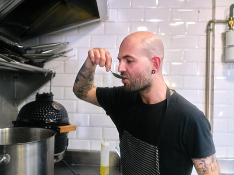 Male chef tasting food with a spoon from a pot while working in a restaurant kitchen