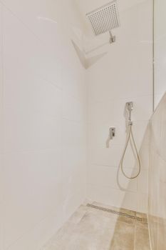 Shower faucets attached to tiled wall near glass partition and ornamental curtail in washroom at home