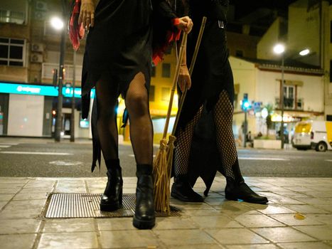 Cropped front view of the legs of two young women dressed as witches for Halloween on the streets of Valencia, Spain.