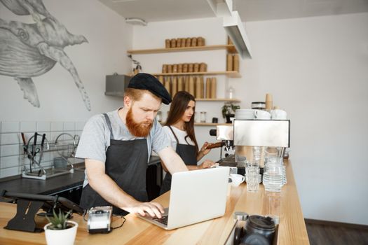 Coffee Business Concept - Young handsome bearded bartender, barista or manager working and planing in laptop at modern coffee shop