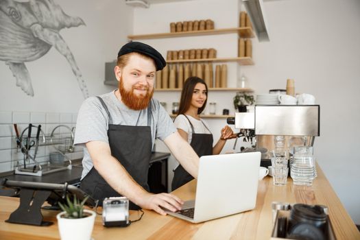 Coffee Business Concept - Young handsome bearded bartender, barista or manager working and planing in laptop at modern coffee shop