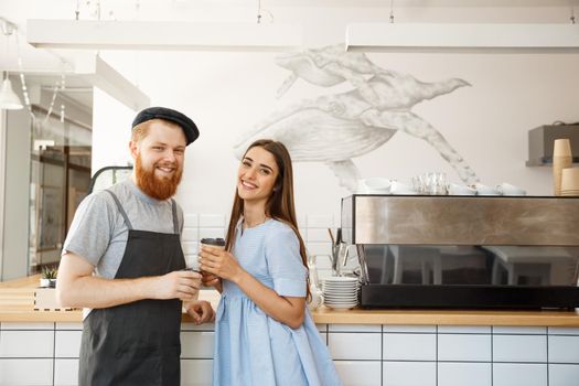 Coffee Business Concept - young smart bearded bartender enjoy talking and giving take away cup of coffee to pretty customer.