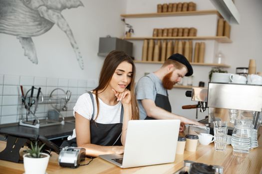 Coffee Business Concept - beautiful caucasian bartender barista or manager working and planing in laptop at modern coffee shop.