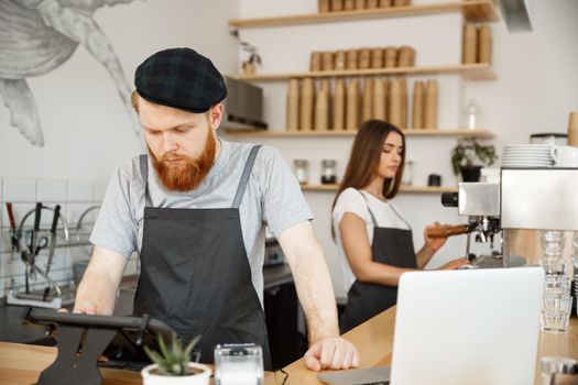 Coffee Business Concept - Young handsome bearded bartende, barista or manager posting the order from guest in digital tablet menu at modern coffee shop.