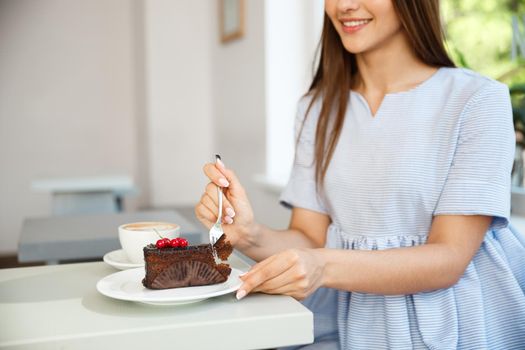 Young attractive Caucasian lady enjoy eating chocolate cake with hot coffee in modern coffee shop at noon.