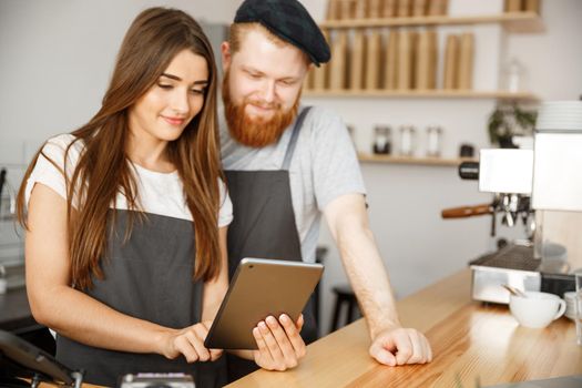 Coffee Business Concept - Satisfied and smile owners couple look on tablet orders online in modern coffee shop