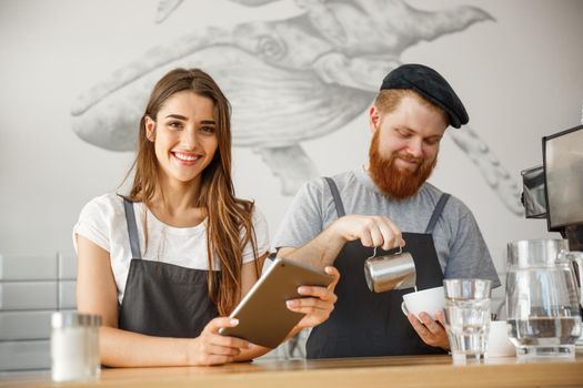 Coffee Business Concept - Cheerful baristas looking at their tablets for online orders in modern coffee shop.