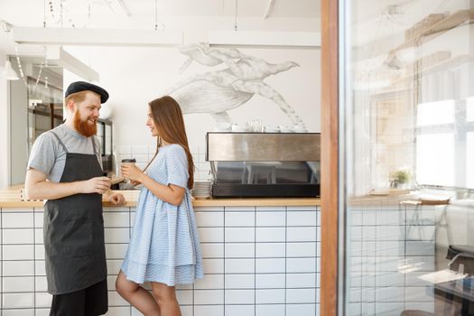 Coffee Business Concept - young smart bearded bartender enjoy talking and giving take away cup of coffee to pretty customer.