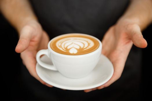 Coffee Business Concept - Cropped Close up of female serving coffee with latte art while standing in coffee shop. Focus on female hands placing a cup of coffee.