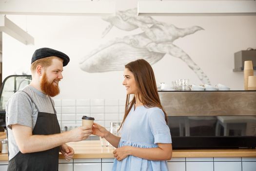 Coffee Business Concept - young smart bearded bartender enjoy talking and giving take away cup of coffee to pretty customer.