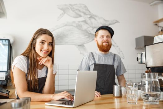 Coffee Business Concept - Cheerful baristas looking at their laptop for online orders in modern coffee shop.