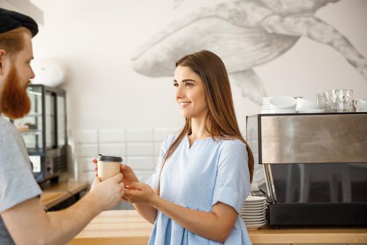 Coffee Business Concept - young smart bearded bartender enjoy talking and giving take away cup of coffee to pretty customer.