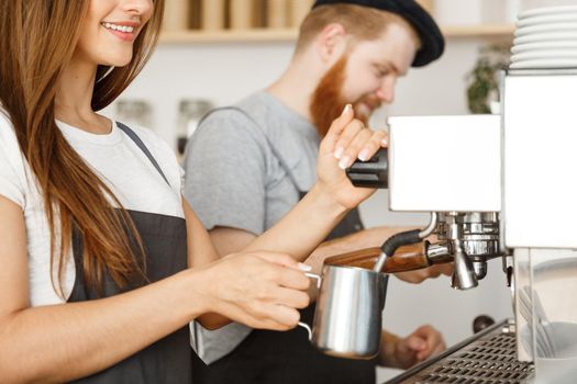 Coffee Business Concept - portrait of lady barista in apron preparing and steaming milk for coffee order with her partner while standing at cafe.