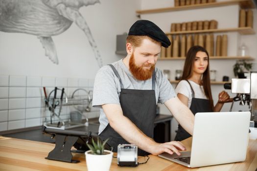 Coffee Business Concept - Young handsome bearded bartende, barista or manager working and planing in laptop at modern coffee shop.