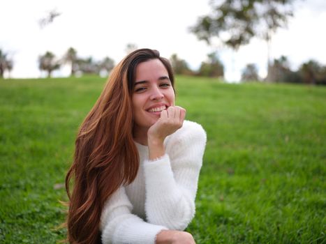 Front view of a young woman in the park happily smiling at the camera with her hand on her chin. Concept of emotions.