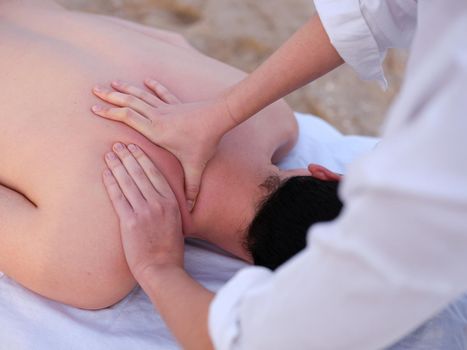 Cropped view of a young man receiving shoulder massage from a young chiromassage therapist on a beach in Valencia.