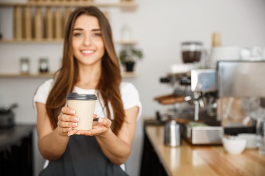 Coffee Business Concept - Beautiful Caucasian lady smiling at camera offers disposable take away hot coffee at the modern coffee shop