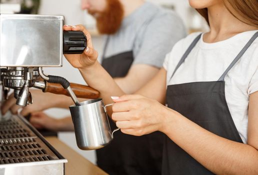 Coffee Business Concept - portrait of lady barista in apron preparing and steaming milk for coffee order with her partner while standing at cafe.