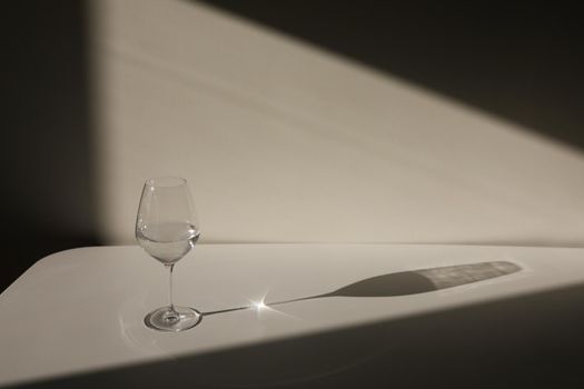 A glass of water on a white background with a shadow. Chiaroscuro from the window. Close-up, copy space.