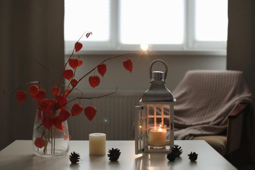 cozy autumn still life, candles, flowers, twigs of orange physalis and details of home interior.