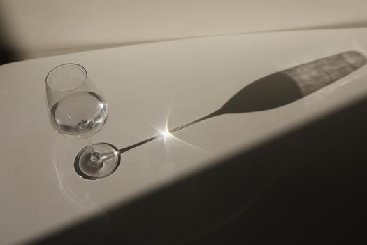 A glass of water on a white background with a shadow. Chiaroscuro from the window. Close-up, copy space.