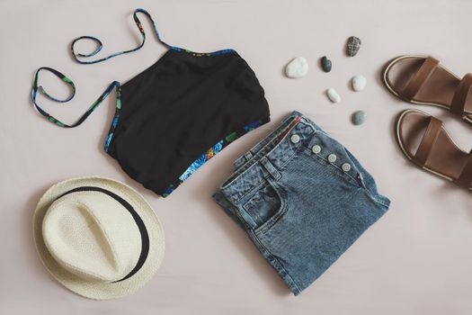 flat lay composition with female top, denim shorts, sandals and a wicker rattan bag on beige background top view.