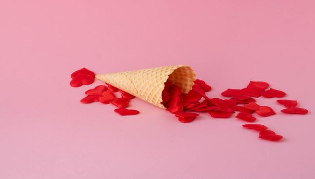 Sweet waffle cone on a pink background with red hearts.