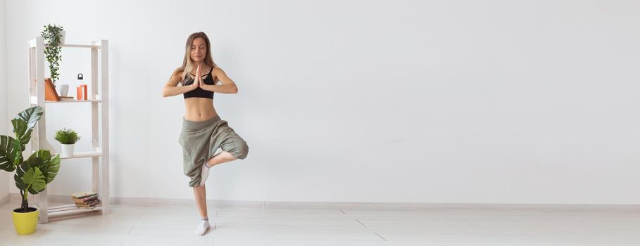 Woman practise yoga performs. Tree pose standing inside cozy room with plants and greenery. Healthy lifestyle and mindfulness banner white background with copy space