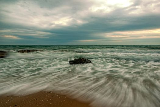 Stunning long exposure seascape with waves flowing between rocks at sunset