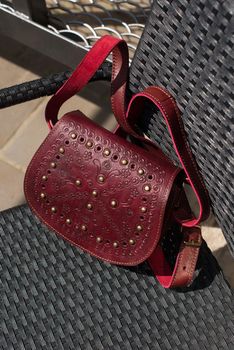 small burgundy women's leather bag with a carved pattern. Outdoor photo.