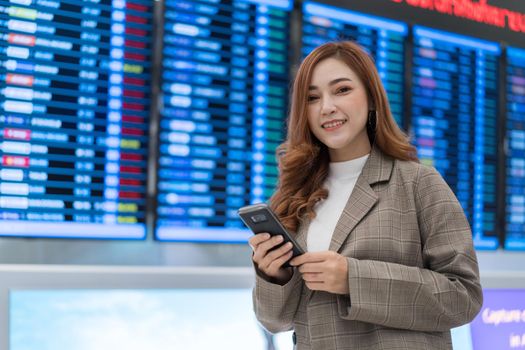 beautiful woman using smartphone with flight information board at airport