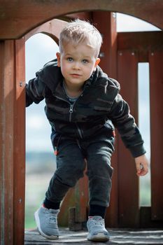 Small boy carefully goes from brown,  wooden playhouse. Cute baby boy in outdoor playground. A jolly childhood time