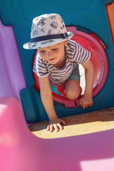 The little boy plays in a colorful, plastic playroom, he performs crawl in tunnel exercises