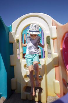 A little boy with a hat climbs a staircase on a colorful plastic playground and performs coordination exercises