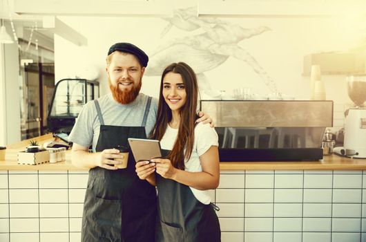 Coffee Business Concept - Cheerful baristas looking at their tablets for online orders