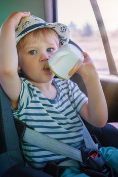 A little boy in a hat and a striped T-shirt travels in the car and drinks juice